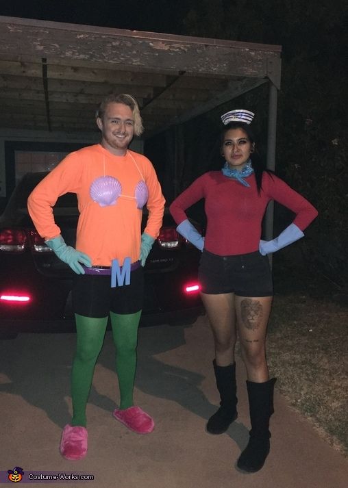 two people in costumes standing next to each other near a car with the headlights on