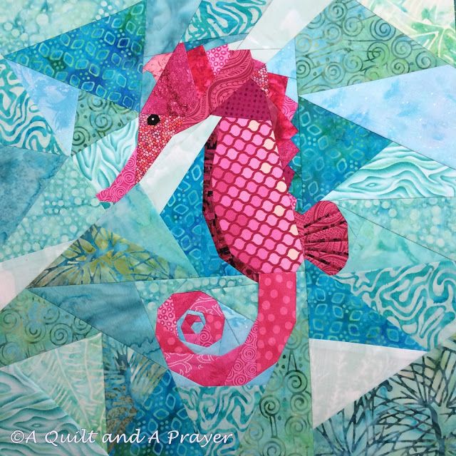 a pink sea horse is sitting on top of a blue and green patchwork quilt