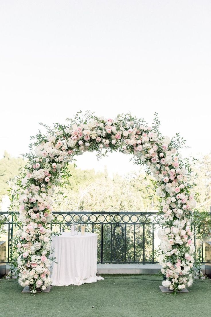 an outdoor ceremony setup with white and pink flowers on the arch over looking the grass