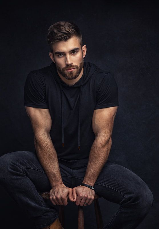 a man sitting on top of a stool with his hands in his pockets and looking at the camera