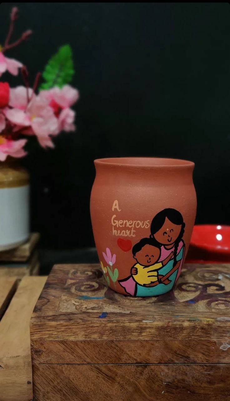 a clay pot with an image of a woman holding a baby on it and pink flowers in the background