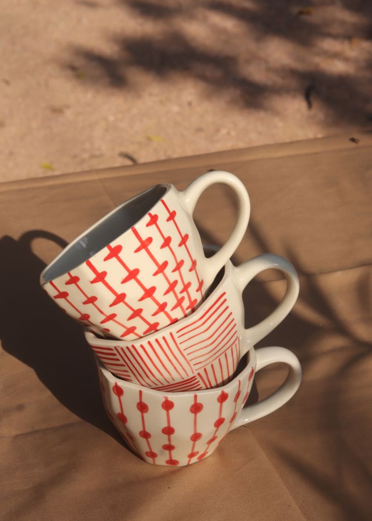 three coffee mugs stacked on top of each other with red crosses painted on them