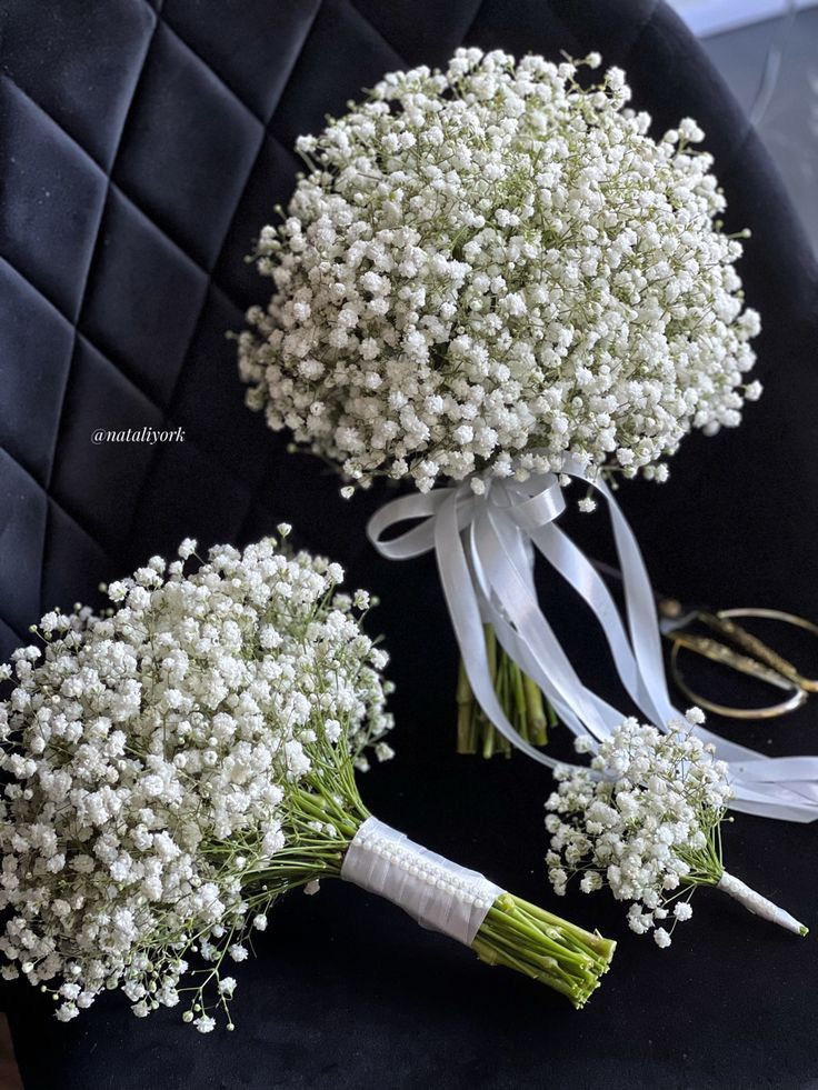 two bouquets of baby's breath are sitting on a black chair with white ribbons