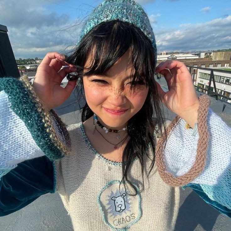 a young woman is posing with her hands on her head and wearing a knitted hat