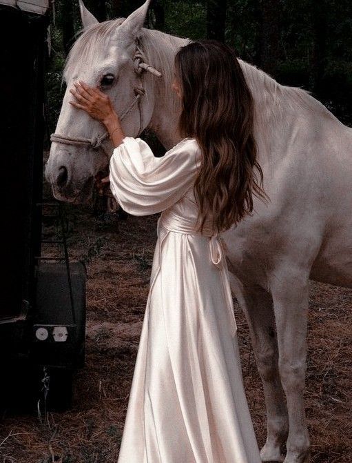 a woman in a white dress standing next to a horse with her hand on it's face