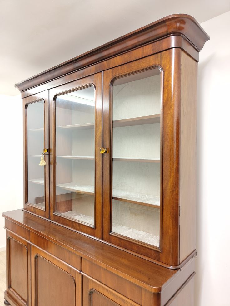 a wooden china cabinet with glass doors and shelves on the front, in a white walled room