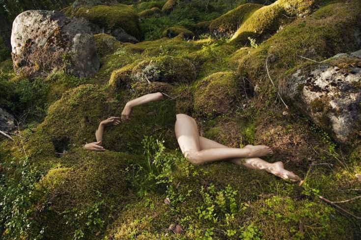 a naked woman laying on the ground covered in moss