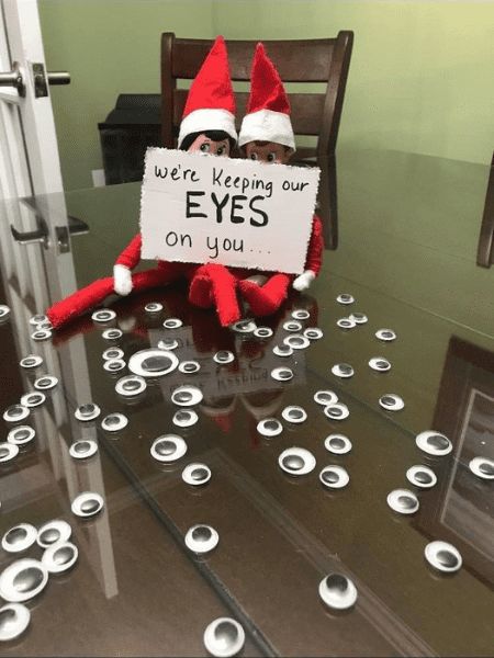 an elf sitting on top of a glass table holding a sign that says, we're keeping our eyes on you