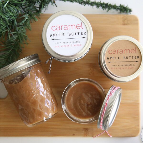 two jars of caramel apple butter on a cutting board next to some pine branches