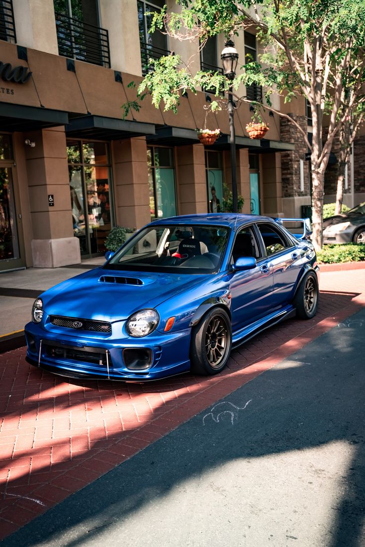 a blue subarunt parked on the side of a road next to a building