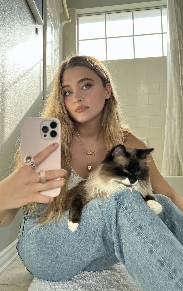 a woman taking a selfie with her cell phone and cat sitting on her lap