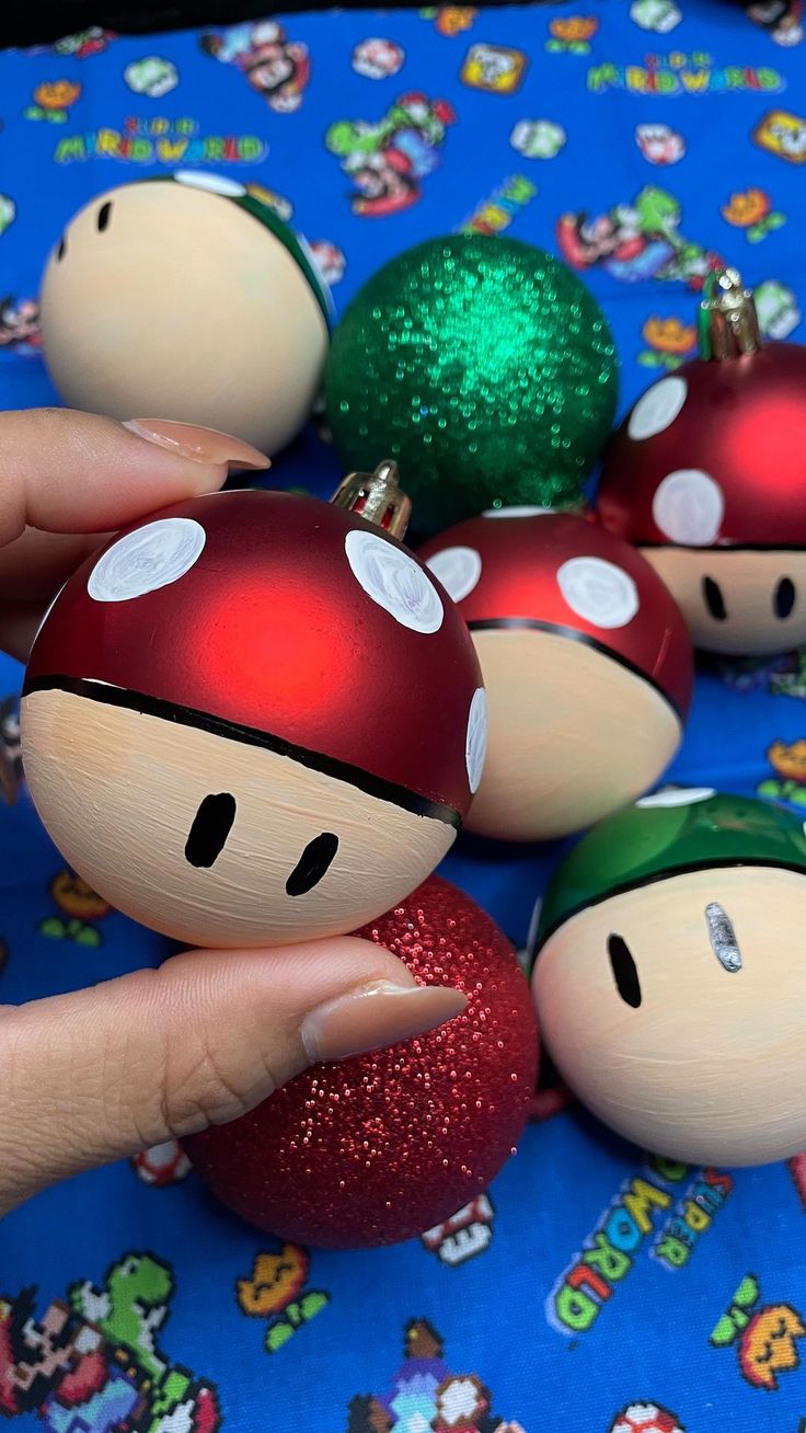 a hand is holding an ornament in front of some christmas ornaments on a table