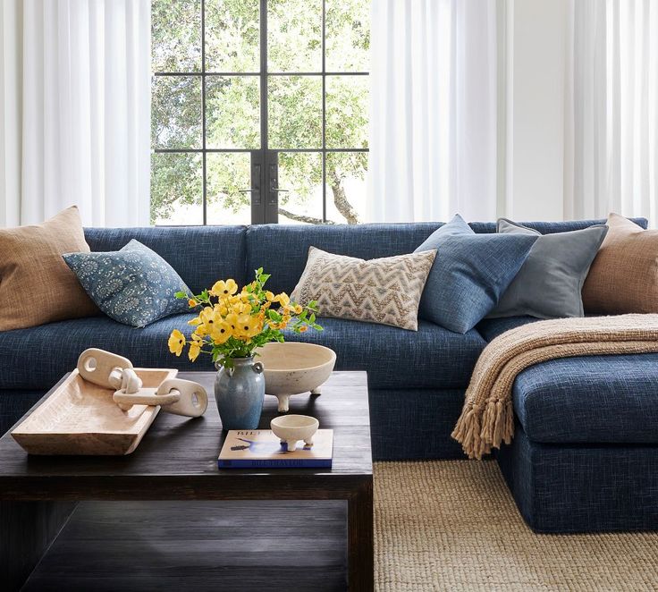 a living room with blue couches and yellow flowers in a vase on the coffee table