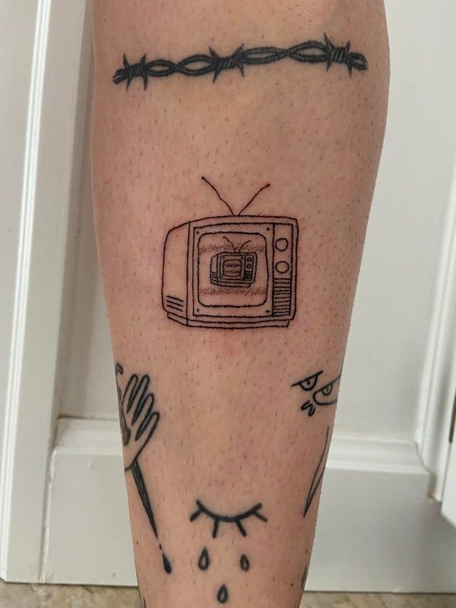 a tattoo on the leg of a person with a tv and barbed wire