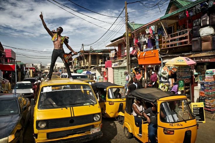 a man standing on top of a yellow car in the middle of a crowded street