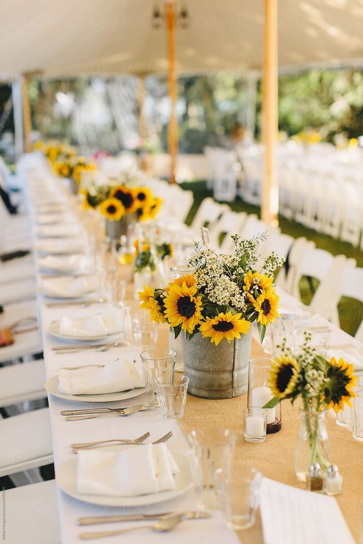 a long table with sunflowers in vases and place settings on the tables