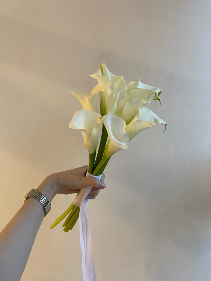 a person holding a bouquet of white flowers in their left hand with a ribbon tied around it