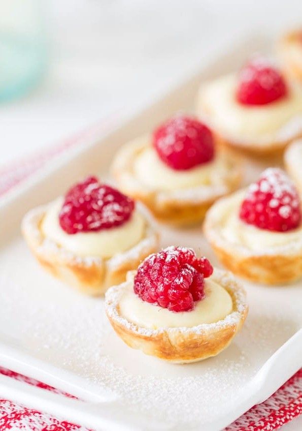 small pastries with raspberry toppings are on a white platter, ready to be eaten