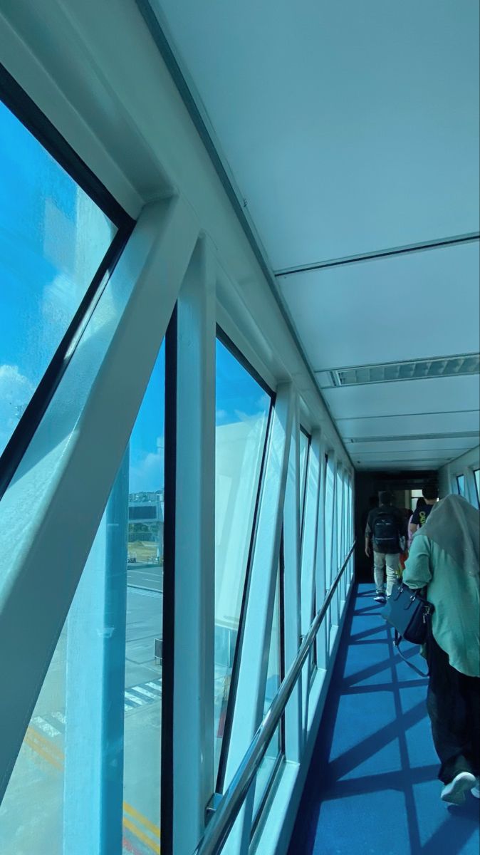 people are walking down the walkway in an airport with large windows on either side of them