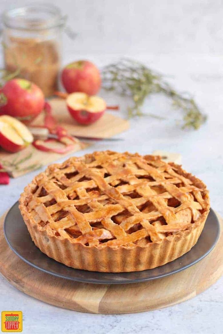 an apple pie on a plate with apples in the background