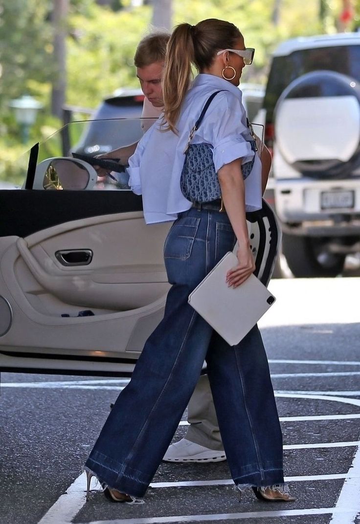 a woman in high waisted jeans is walking towards a car with her handbag