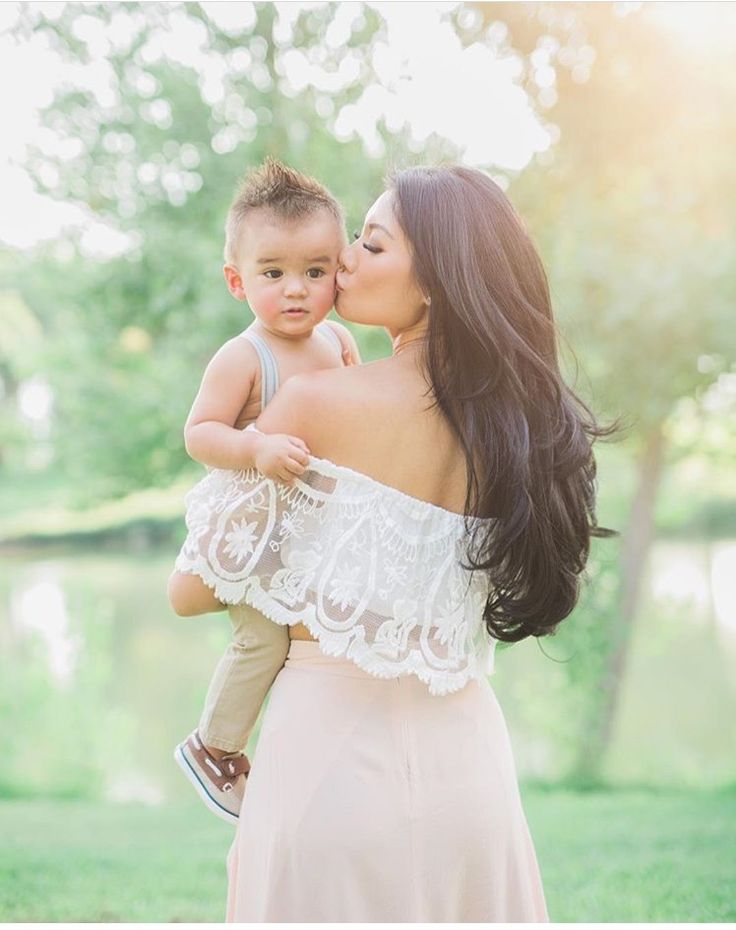 a woman holding a young boy in her arms and kissing him with the sun shining behind them