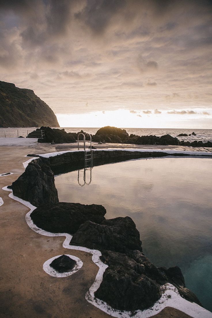 a body of water sitting on top of a sandy beach next to the ocean under a cloudy sky