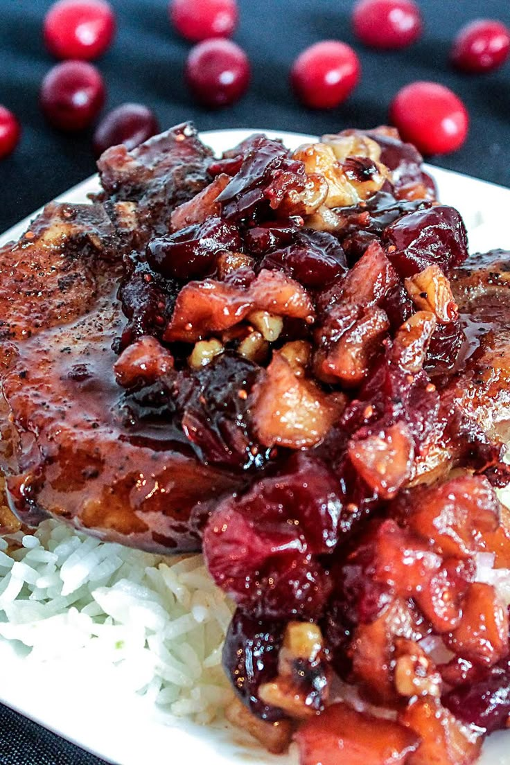 a white plate topped with meat covered in cranberry sauce next to rice and cherries