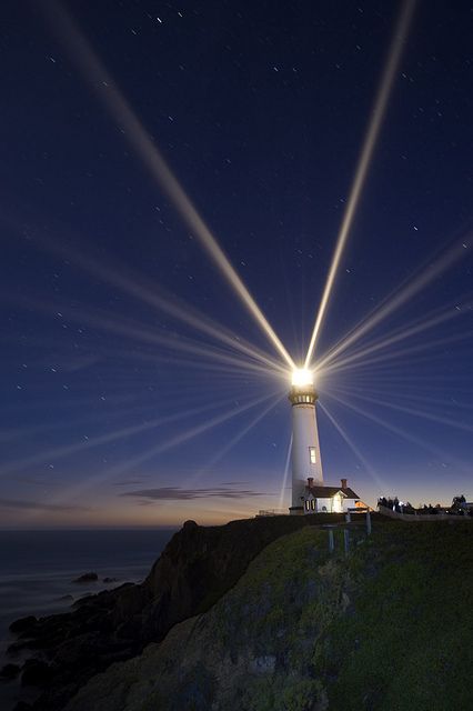 a light house is lit up at night on the edge of a cliff by the ocean