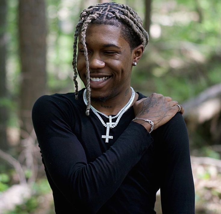 a man with dreadlocks standing in the woods and smiling at the camera while wearing a black shirt