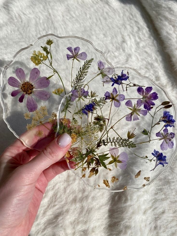 a hand holding a glass plate with pressed flowers on it