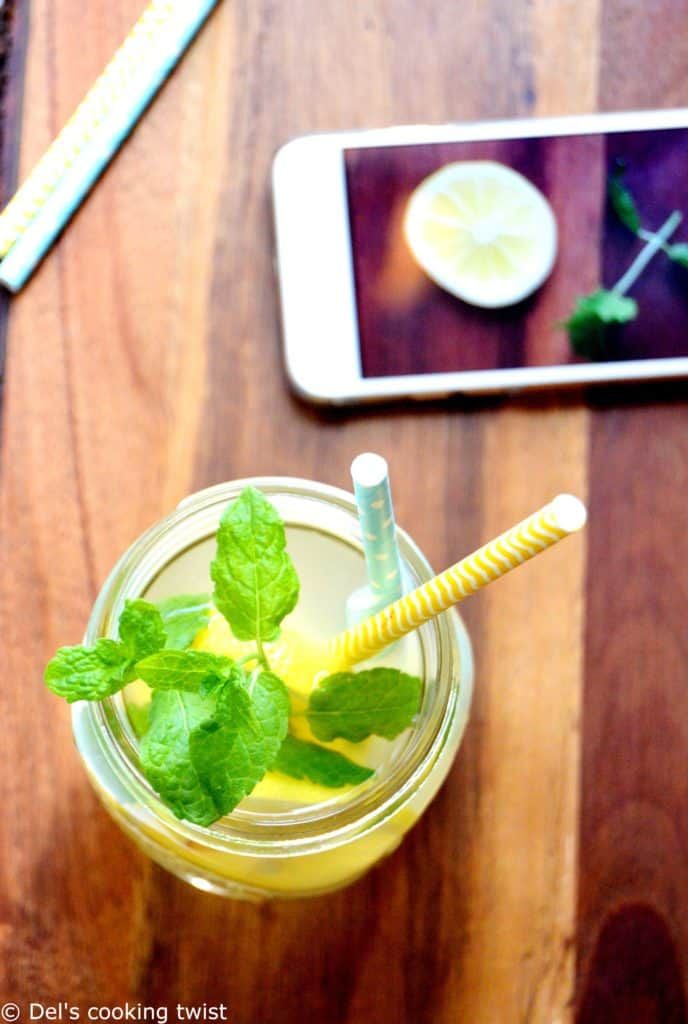 a glass filled with lemonade and mint on top of a wooden table next to a cell phone