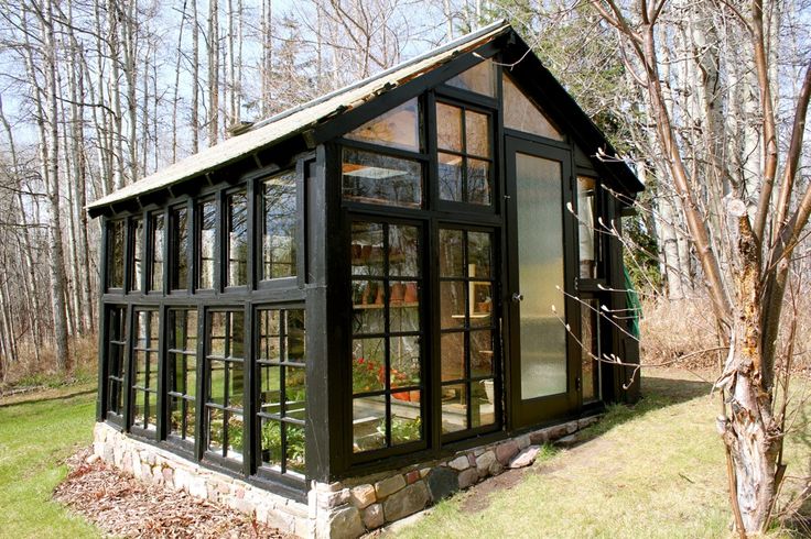 a small black cabin in the woods with lots of windows