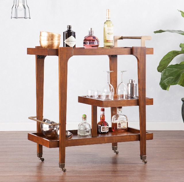 a wooden bar cart filled with bottles and glasses on top of a hard wood floor