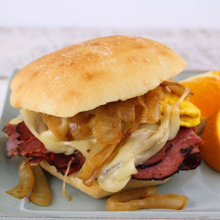 a sandwich with meat, cheese and onions on a blue plate next to an orange