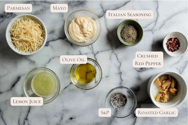 the ingredients for an italian salad laid out on a marble counter top, including olives, parmesan cheese, lemon juice, and mayo