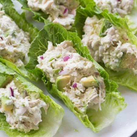 several lettuce wraps with chicken salad on them sitting on a white platter