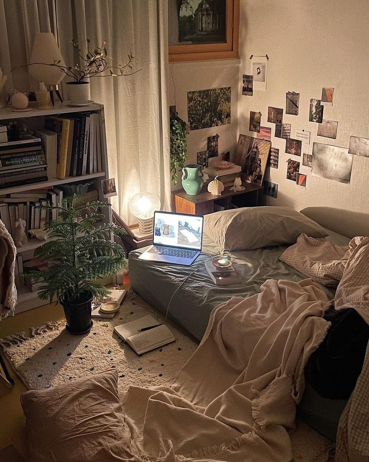 a laptop computer sitting on top of a bed next to a plant in a pot