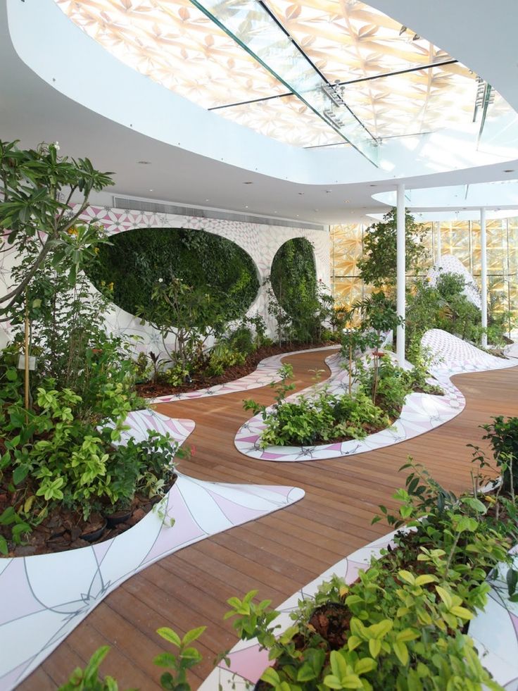 an indoor garden is shown with trees and plants in white pots on the floor, along with wooden walkways