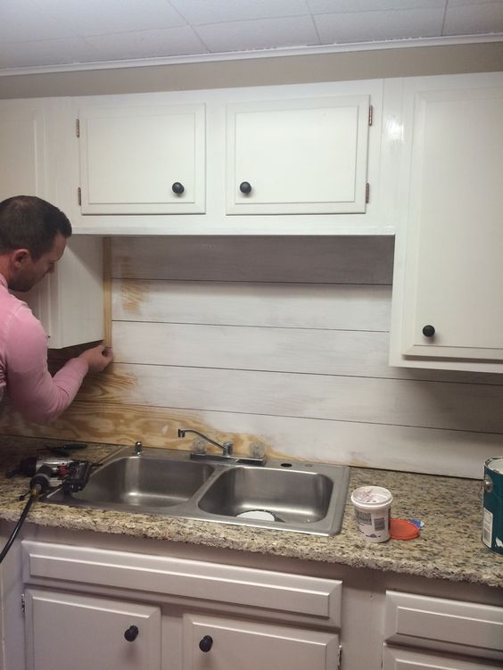 a man in pink shirt working on a kitchen counter with wooden planks and white cabinets