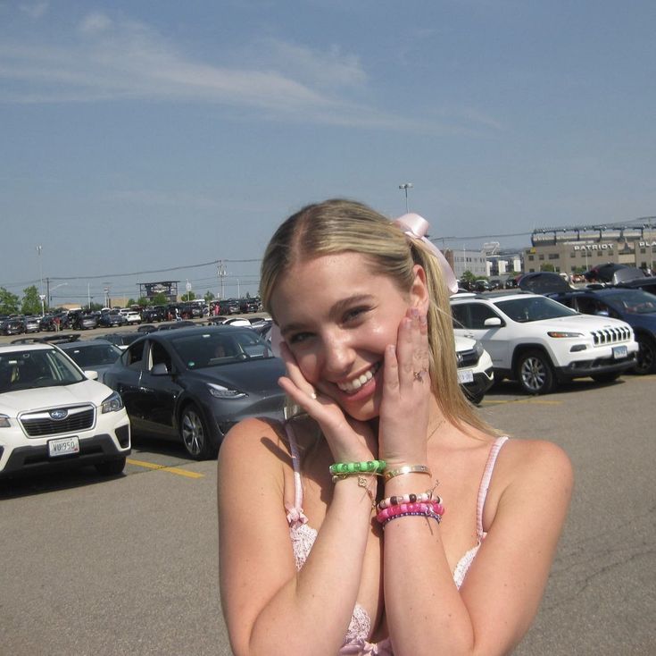 a girl in a parking lot holding her hand up to her face and smiling at the camera