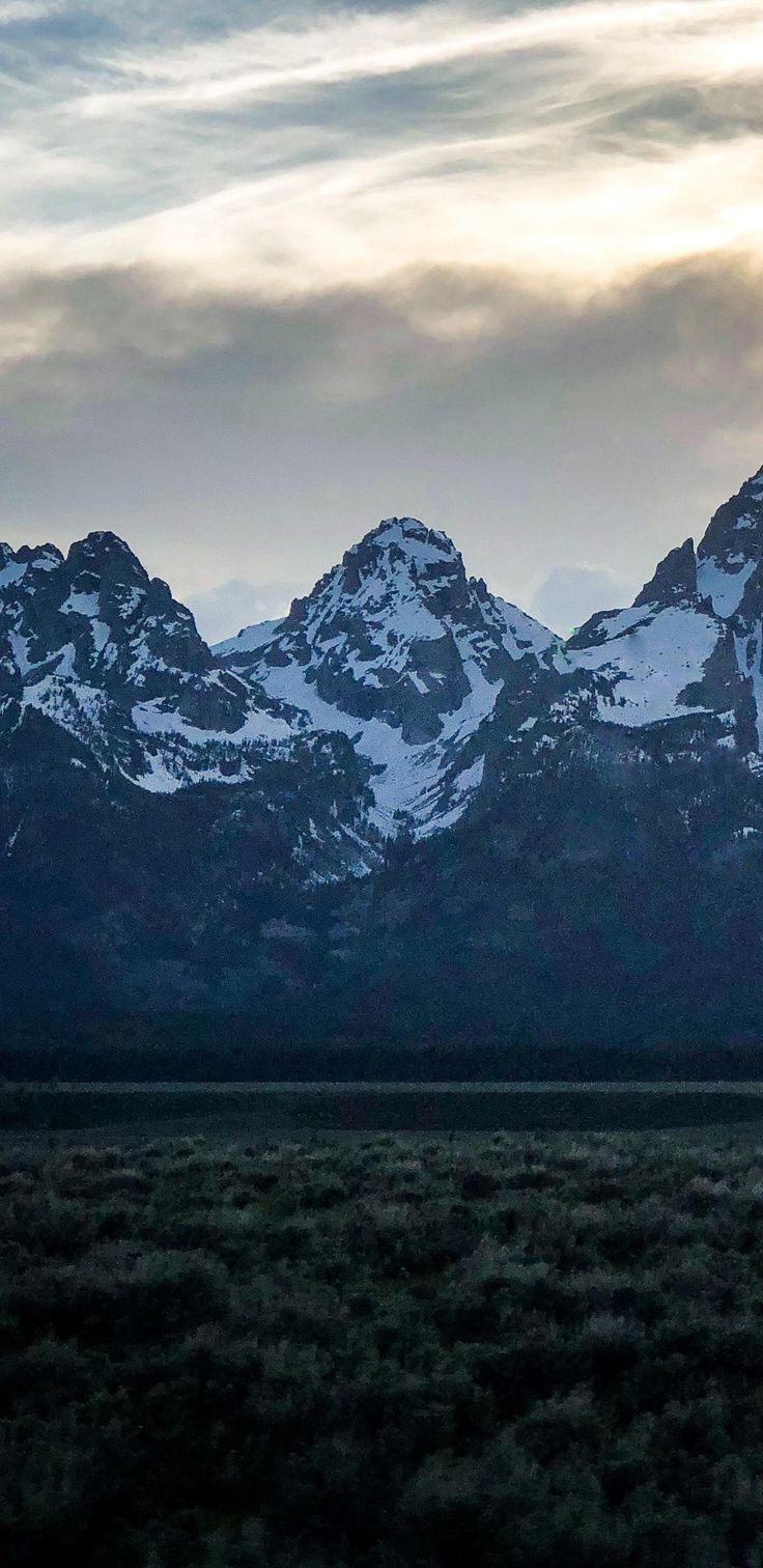 the mountains are covered in snow as the sun is low to the ground and dark clouds can be seen above them