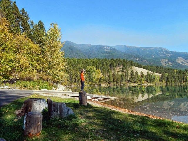 a lake surrounded by trees and mountains in the background with a person standing next to it