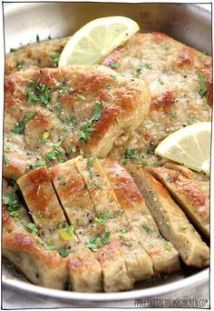 sliced pork chops in a skillet with lemon wedges and parsley on top