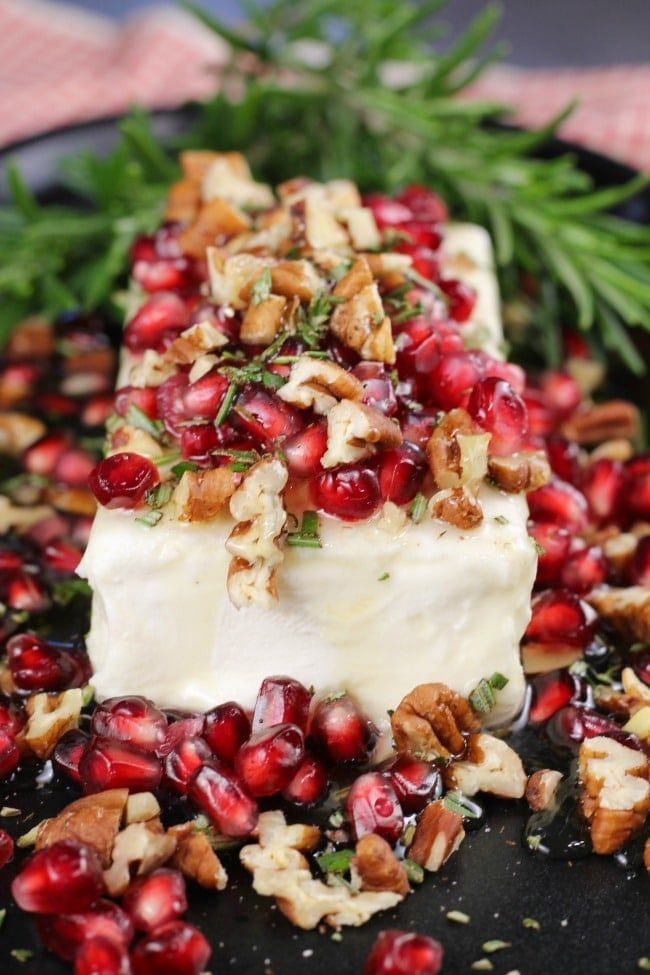 a black plate topped with cheese covered in pomegranate