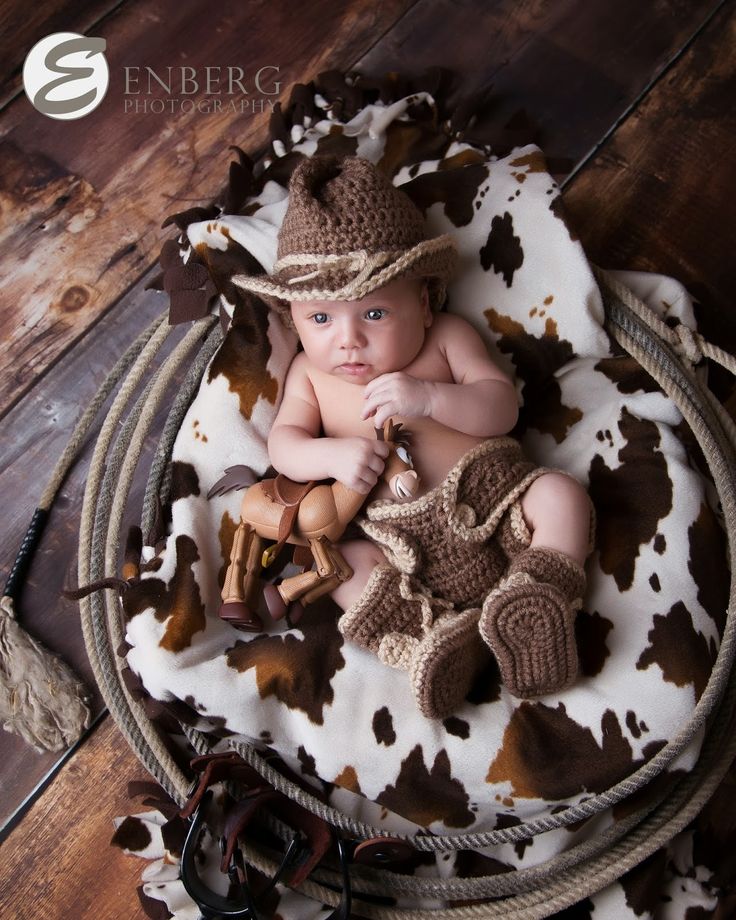 a baby in a cowboy hat laying on top of a cow print blanket and holding a stuffed animal