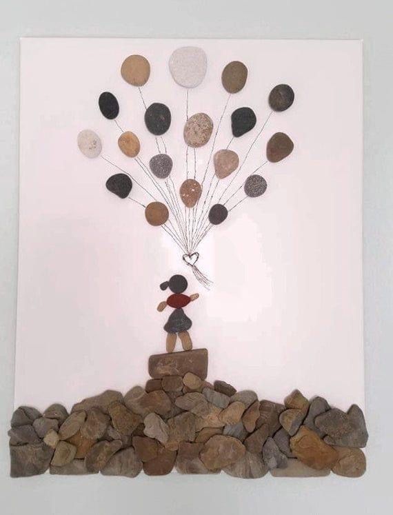 a sculpture made out of rocks and stones with a person holding a bunch of balloons