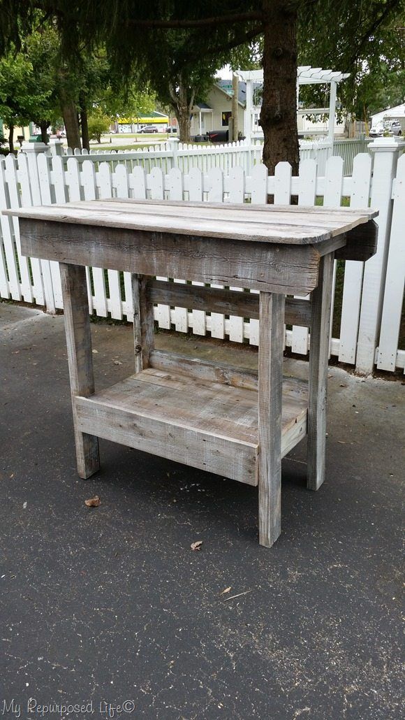 an old wooden table sitting in front of a white picket fence