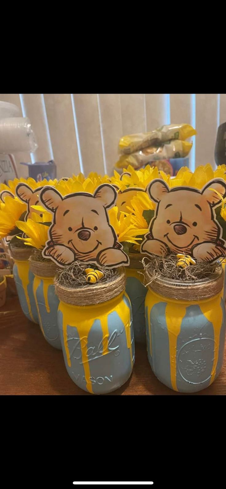 mason jars filled with yellow flowers and teddy bears on top of each jar are the centerpieces for this baby's first birthday party