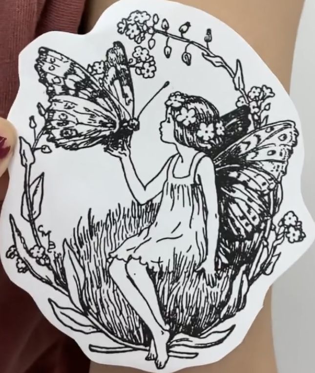 a woman holding up a sticker with a drawing of a fairy sitting on it